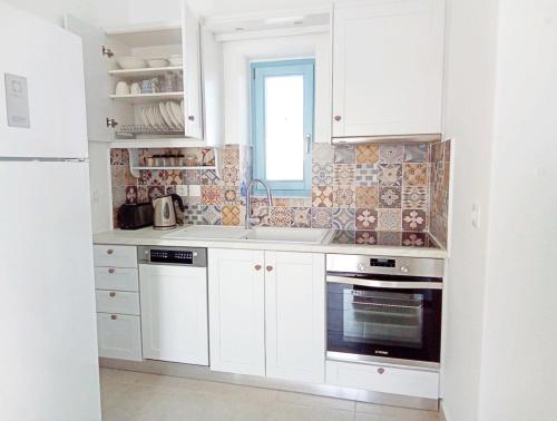 a kitchen with white cabinets and a sink and a window at Aeriko Apartment in Paros in Dhragoulás