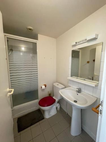 La salle de bains est pourvue d'un lavabo et de toilettes avec un siège rouge. dans l'établissement Studio, hyper centre La Rochelle, à La Rochelle