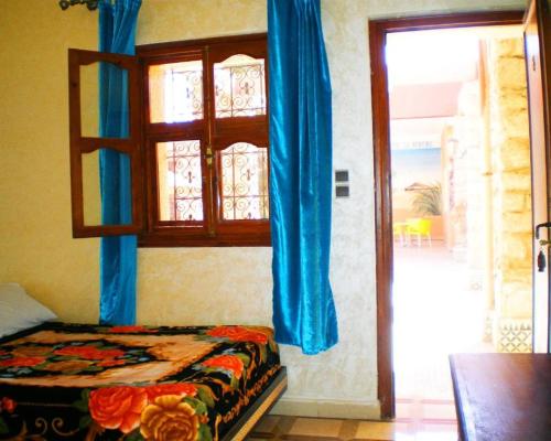 Schlafzimmer mit einem Bett und einem Fenster mit blauen Vorhängen in der Unterkunft TIRIKA Hôtel La Gazelle in Zemmour Touirza