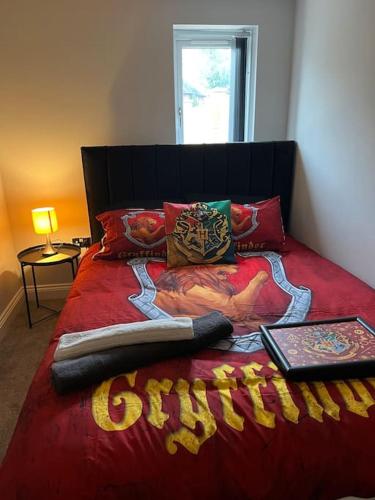 a bed with a red comforter with a book on it at Potters Retreat- Warner Bros Studios and London in Watford