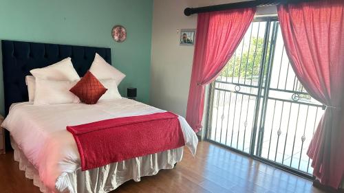 sypialnia z łóżkiem z czerwonymi zasłonami i dużym oknem w obiekcie Nyasa Villa w mieście Southgate