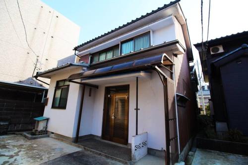 a small white house with a door on a street at 福井駅裏ハウス325貸切民泊 一日一組限定 駅から徒歩7分家族連れ団体様歓迎 安い in Fukui
