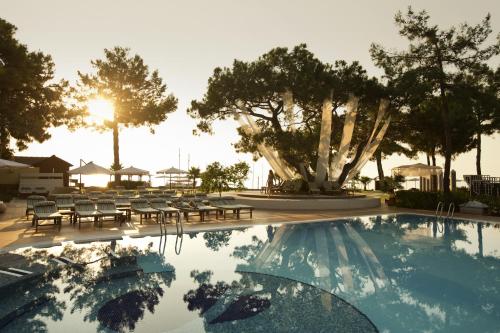 una piscina con sillas, una mesa y árboles en ROBINSON CAMYUVA - Adults only en Kemer