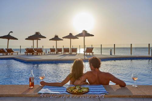 a man and a woman sitting next to a swimming pool at Universal Hotel Cabo Blanco - Adults Only in Colonia Sant Jordi