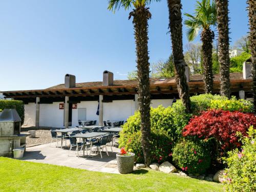 a patio with tables and chairs and palm trees at Apartment Villaggio Sureggio A7 mit TicinoTicket by Interhome in Lugaggia