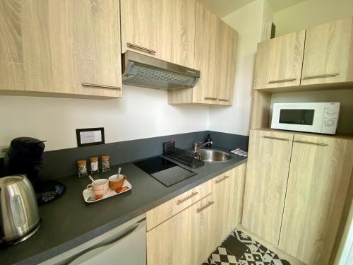 Una cocina con armarios de madera, fregadero y microondas. en Superbe appartement confortable, proche centre ville, en Rennes
