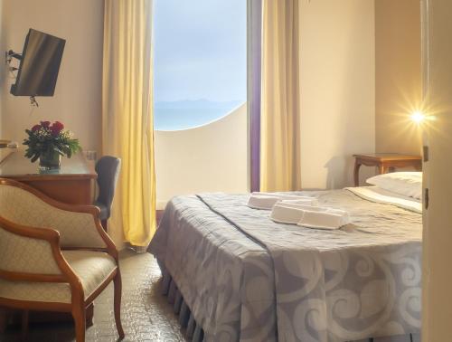 una camera d'albergo con un letto, una sedia e una finestra di Hotel Sinuessa Terme a Mondragone