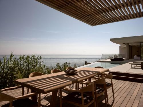 a wooden table and chairs on a deck with the ocean at Opsis villas, A waterfront & architectural retreat in Akrotiri