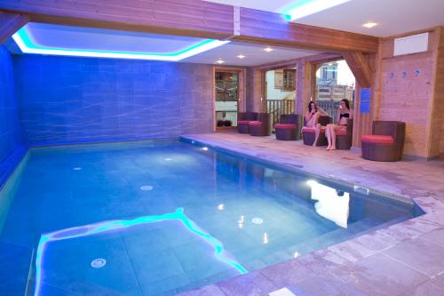 - une piscine avec 2 personnes assises dans des chaises à côté dans l'établissement Chalet familial La Griotte avec piscine, à Praz-sur-Arly