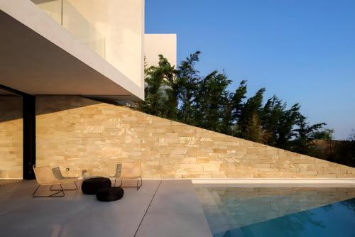 a house with a swimming pool next to a stone wall at Opsis villas, A waterfront & architectural retreat in Akrotiri