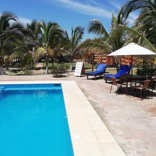 a swimming pool with a table and chairs and palm trees at Punta Pacífico Bungalows Máncora in Máncora