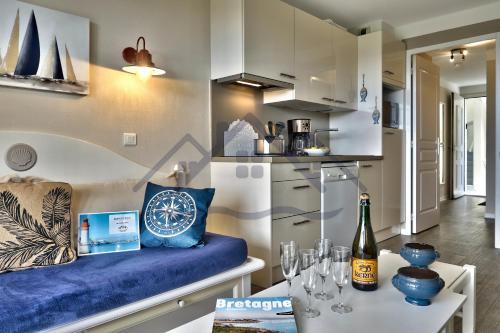 une cuisine avec un canapé bleu et une table avec des verres à vin dans l'établissement LocaLise - A18 - Appartement avec balcon - Petite vue mer à travers le palmier - Piscine de avril à septembre - Wifi inclus - Animaux admis - Draps inclus - Parking inclus, au Guilvinec