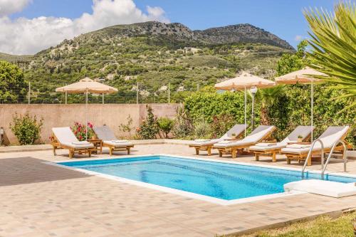 a pool with chairs and umbrellas with a mountain in the background at Villa Skala View in Skala Kefalonias