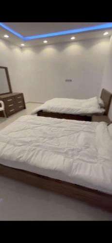 1 dormitorio con 2 camas blancas y luz azul en الفهد, en Mogayra