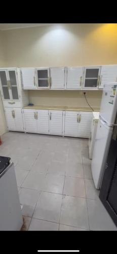 a kitchen with white cabinets and a white tile floor at الفهد in Mogayra