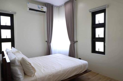 a bedroom with a white bed and two windows at Cozy Pool Villa near SM Pampanga and Sky Ranch Pampanga in San Fernando