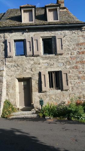 Cette ancienne maison en pierre est dotée d'une porte et de fenêtres blanches. dans l'établissement L'AUBRIETE, à Recoules-dʼAubrac