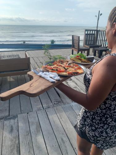 una mujer sosteniendo una bandeja de pizza en una mesa cerca de la playa en Casa heysol en Bahía de Caráquez