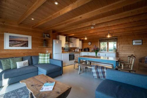 a living room with blue couches and a kitchen at Wood Cabin 2 At Tapnell Farm in Yarmouth