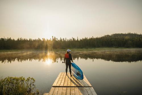 a person standing on a dock with a canoe on a lake at Auberge de Montagne des Chic-Chocs Mountain Lodge - Sepaq in Sainte-Anne-des-Monts