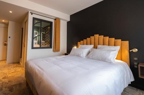 a bedroom with a large white bed with a black wall at Hôtel Les Pins in Saint-Trojan-les-Bains