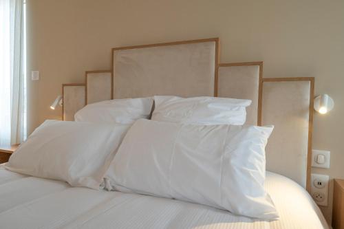 a bed with white sheets and pillows on it at Hôtel Les Pins in Saint-Trojan-les-Bains