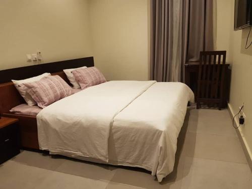 een slaapkamer met een groot bed met witte lakens en roze kussens bij Krotia Lodge Atimpoku 