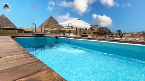 a swimming pool with an umbrella and the pyramids at Pyramids Height Hotel & Pyramids Master Scene Rooftop in Cairo