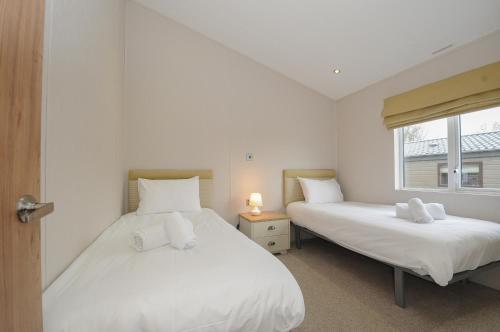 two beds in a white room with a window at Lodge 74 at Riviera Bay Coastal Retreat in Brixham