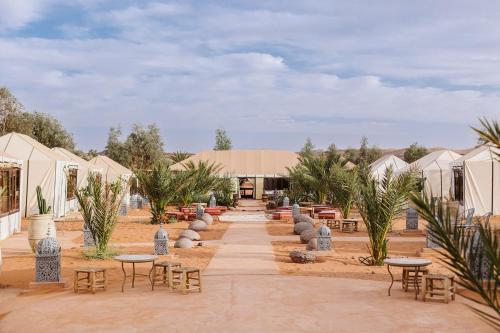 un patio con mesas, sillas y tiendas de campaña en Caravanserai Luxury Desert Camp, en Merzouga