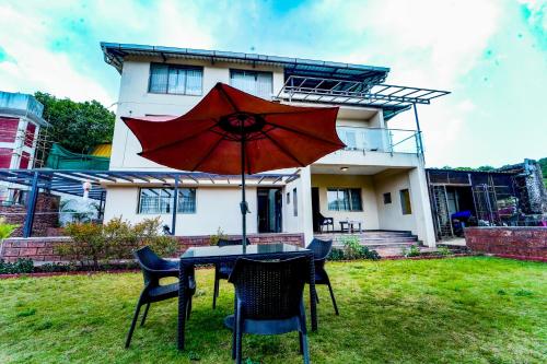a table with an umbrella in front of a house at Hotel Strawberry inn, Mahabaleshwar in Mahabaleshwar