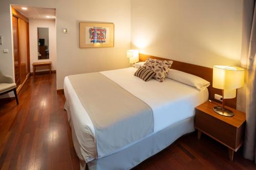 a bedroom with a large white bed and a lamp at Hotel Puente de Alconétar in Garrovillas