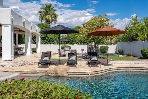 a patio with chairs and umbrellas next to a pool at Two Separate Game Rooms, Heated Pool, Spa, B-ball Court in Mesa