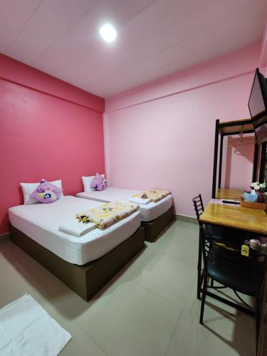 two beds in a room with pink walls and a desk at ลิตเติ้ลโฮม ที่พักเพชรบุรี in Phetchaburi