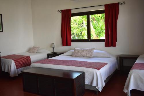 1 dormitorio con 2 camas y una ventana con cortinas rojas en Casa Kiin, en Chichimilá