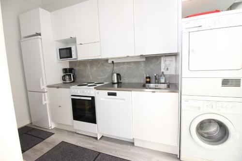 cocina con armarios blancos, lavadora y secadora en Stay Here Apartment Liisa, en Helsinki