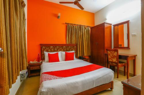 チェンナイにあるCollection O Mamieyaar Veeduのオレンジ色の壁のベッドルーム1室、赤い枕付きのベッド1台が備わります。