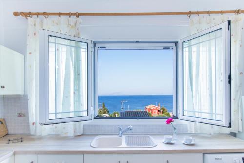 a kitchen with two windows and a sink with a view of the ocean at Apartments MARGARITA Kaizer Bridge in Achílleion