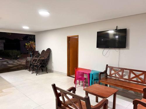 Habitación con sillas, mesas y TV en la pared. en Casa em Campo Grande com piscina en Campo Grande