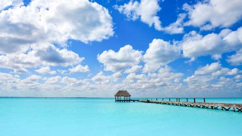 a pier in the water with a blue sky and clouds at Casa aloha-Isla Holbox in Holbox Island