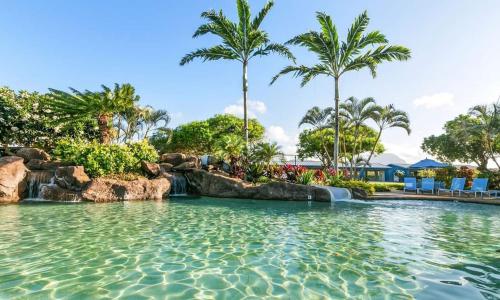 a pool at a resort with a waterfall and palm trees at Kiahuna 106 - Ocean View in Kipu