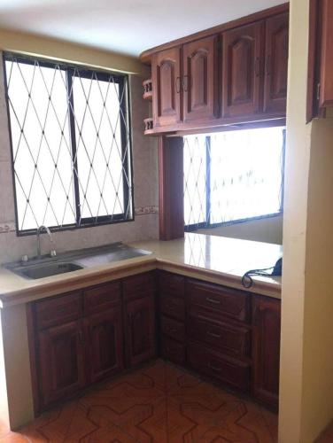 cocina con armarios de madera, fregadero y 2 ventanas en Rio habitaciones en Riobamba