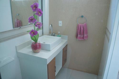 a bathroom with a sink and a vase with purple flowers at Casa na praia recanto de itaipuaçu in Itaipuaçu