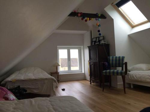 Cette chambre mansardée comprend un lit, une chaise et une fenêtre. dans l'établissement Familly Home, à Grandcamp-Maisy