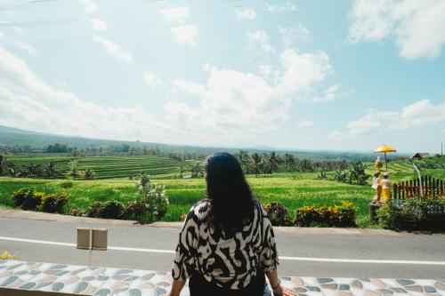 a woman standing on the side of a road looking at a field at Bhuana Agung Villa and Restaurant in Jatiluwih