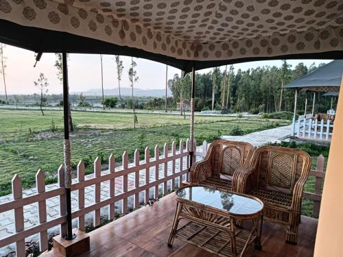 eine Veranda mit 2 Stühlen, einem Tisch und einem Zaun in der Unterkunft Pulastya Wellness Resort in Saharanpur