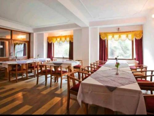 uma sala de jantar com mesas, cadeiras e janelas em Hotel Tara Regency - A family Hotel em Shimla