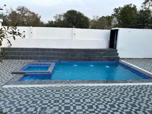 una piscina de agua azul y una valla blanca en namastay farm, en Jaipur