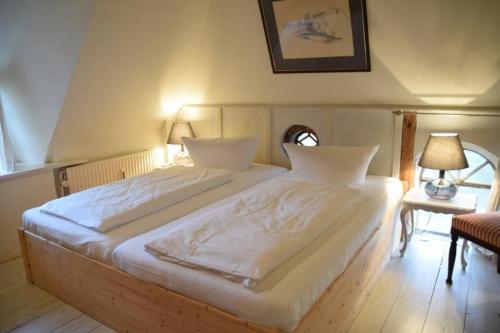 um quarto com uma cama grande e lençóis brancos em Gemütliche Friesenhaushälfte unter Reet über 3 Etagen mit ca. 90 qm. em Westerland