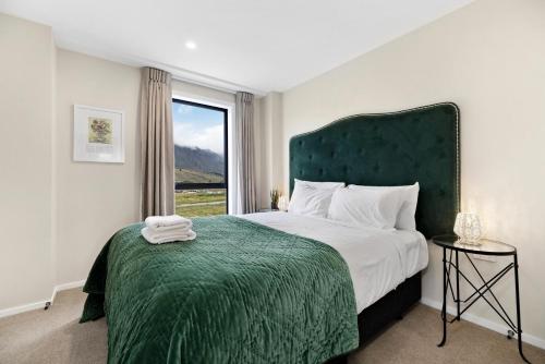 a bedroom with a bed with a green headboard and a window at O'Mera Luxury Retreat in Queenstown